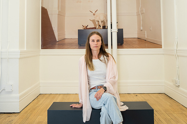 Artist Sage Szkabarnicki-Stuart sitting in front of her photo of baby goats