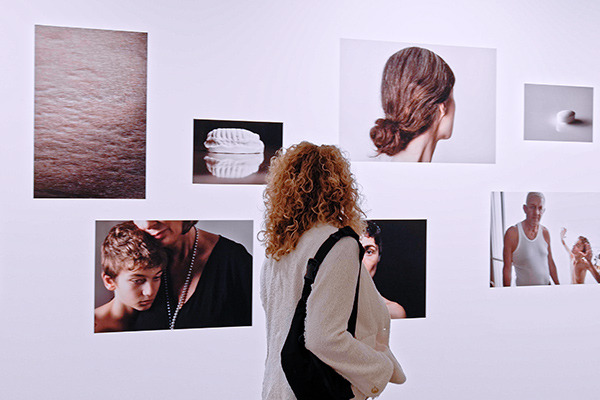 Installation view of Elinor Carucci's photographs, a woman in the foreground looks at the photos